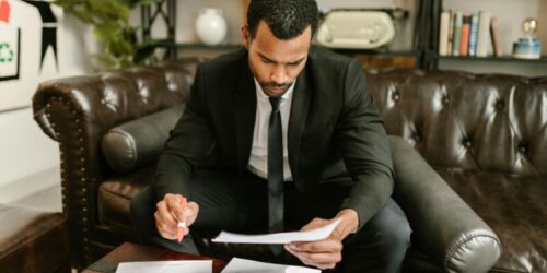 Photo by RDNE Stock project A businessman in a suit attentively reviews paperwork on a brown leather sofa.
