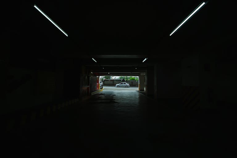 A dimly lit underground parking space opening to a bright street view.