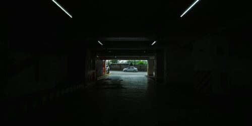 Photo by Nothing Ahead A dimly lit underground parking space opening to a bright street view.