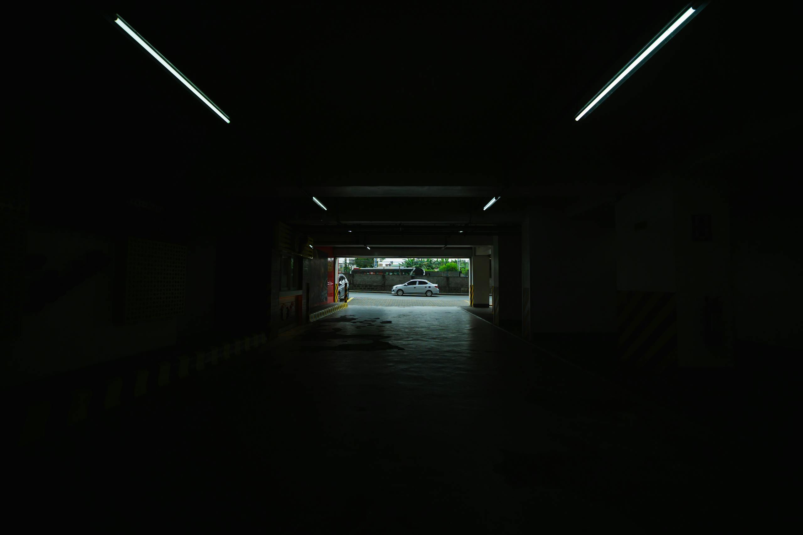 A dimly lit underground parking space opening to a bright street view.