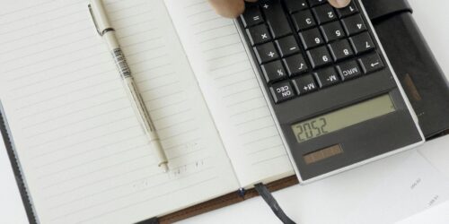 Photo by Hanna Pad A hand using a calculator with financial documents and notebook, depicting an office setup for financial analysis.