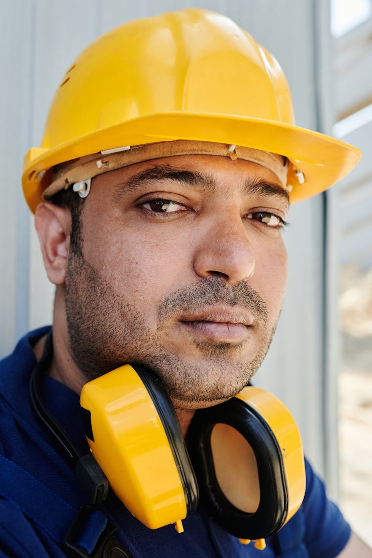 Close-up of a construction worker wearing a yellow hard hat and ear protection outdoors.